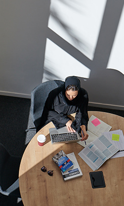  A woman researching on business set-up on her laptop & books at Dubai Outsource City